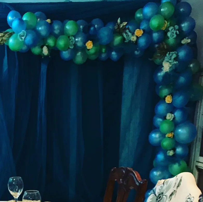 Blue and green organic balloon garland with roses framing a draped backdrop
