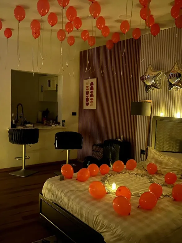 Room decorated with orange balloons on the ceiling and a balloon heart on the bed